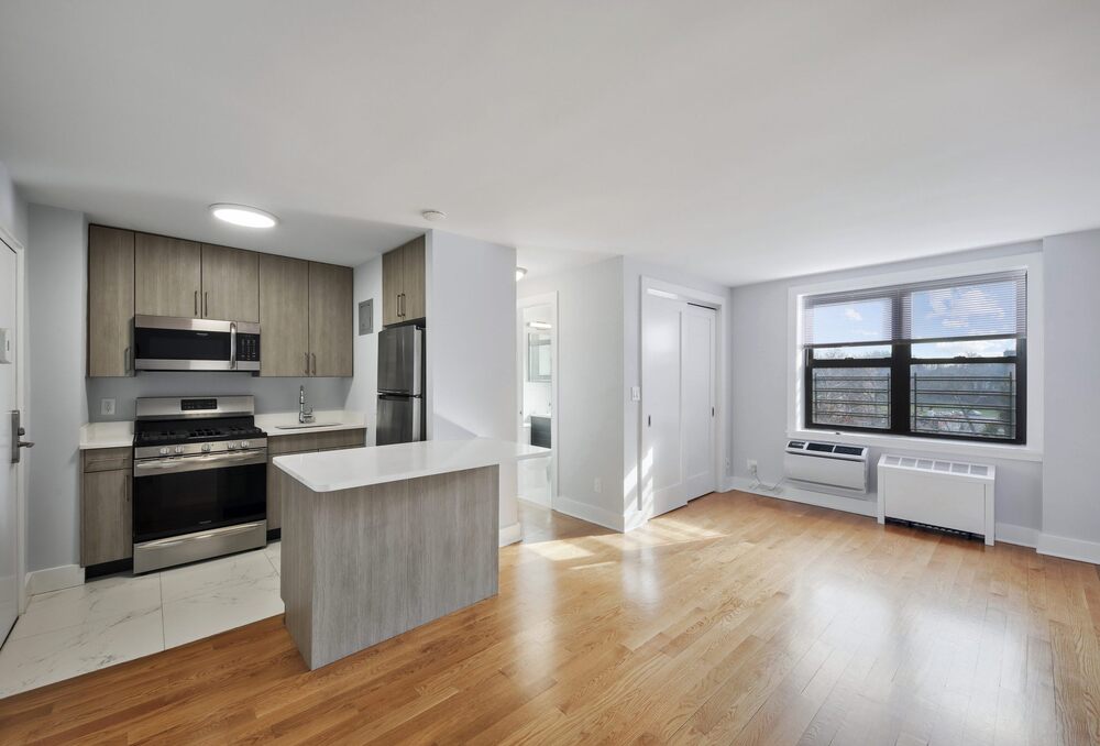 an empty living room with a kitchen and a large window